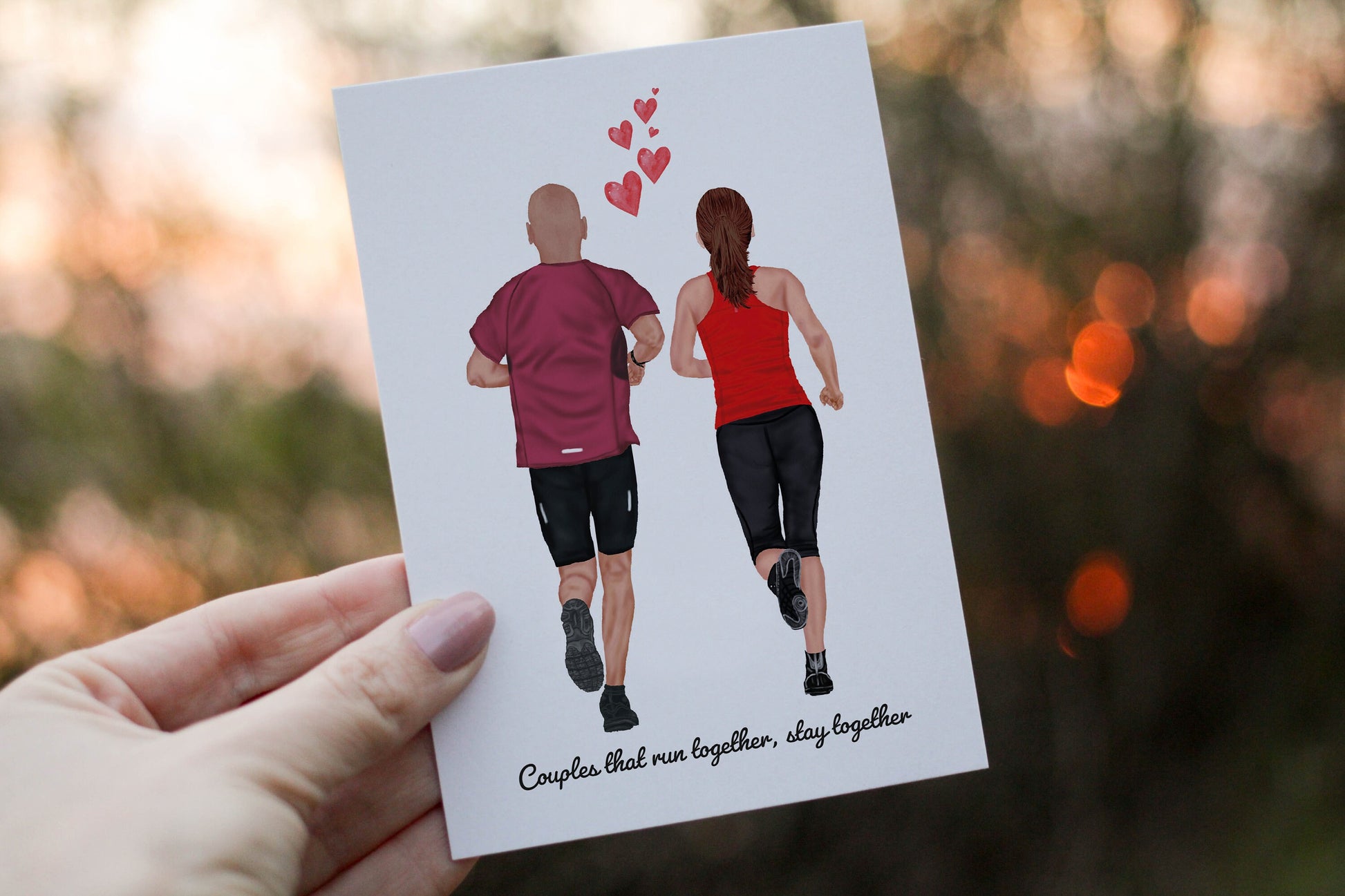 Card with illustration of a couple running and hearts, held by a hand outdoors.