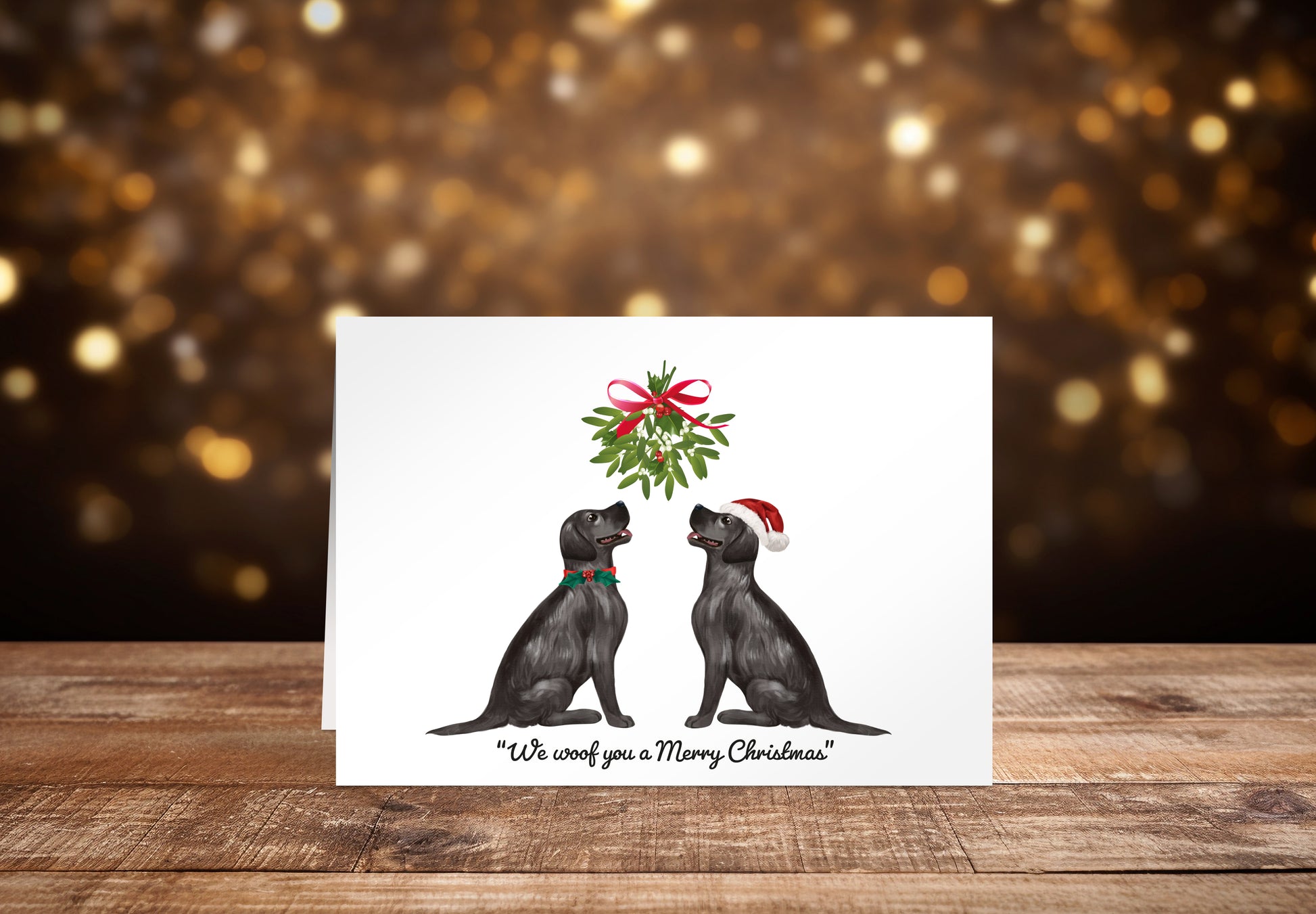 Christmas card with two black Labrador dogs sitting underneath a mistletoe wreath on a white background, with the text: "We woof you a Merry Christmas"