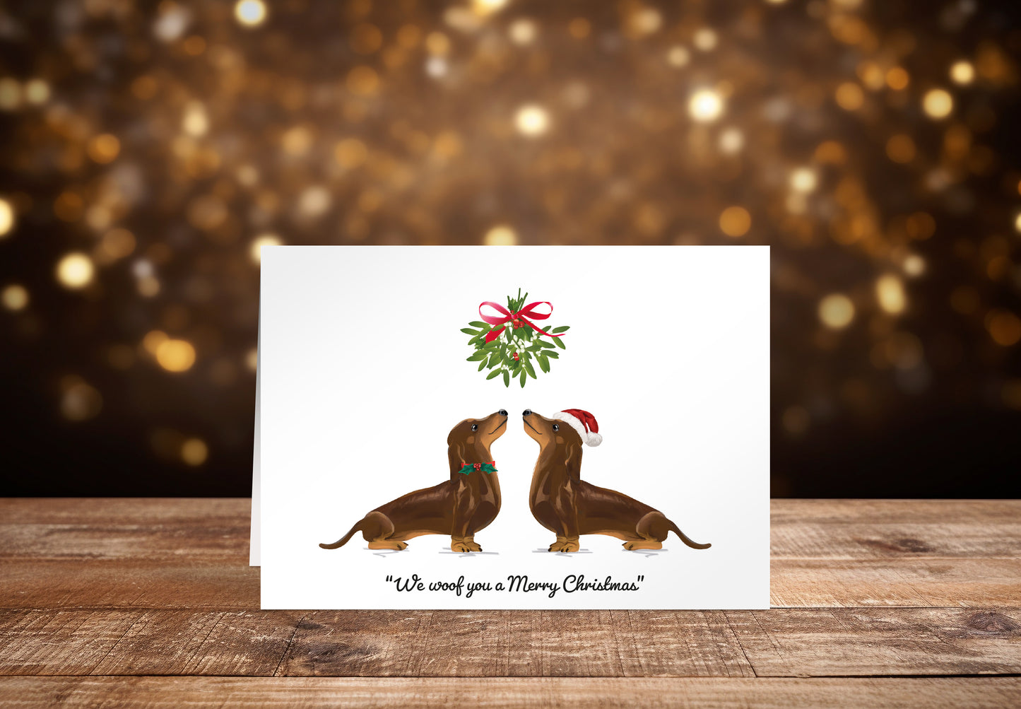 Christmas card with two brown Dachshund dogs underneath mistletoe on a white background with the text "We woof you a Merry Christmas" underneath. 