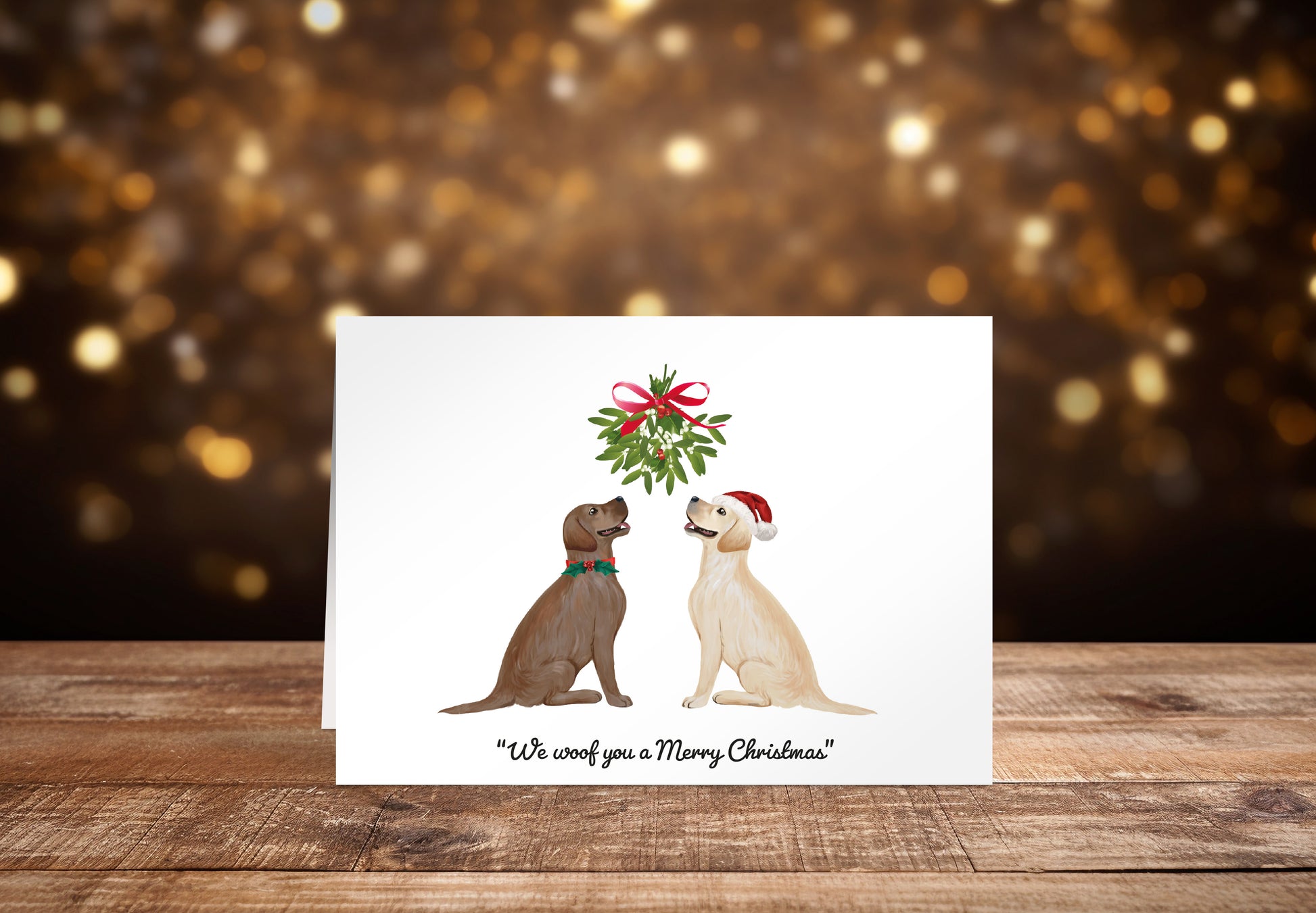 Christmas card with a brown and a cream Labrador dog sitting underneath a mistletoe wreath on a white background, with the text: "We woof you a Merry Christmas"