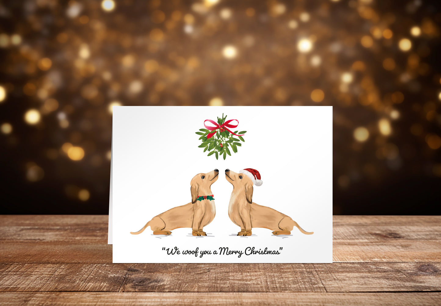 Christmas card with two cream Dachshund dogs underneath mistletoe on a white background with the text "We woof you a Merry Christmas" underneath. 