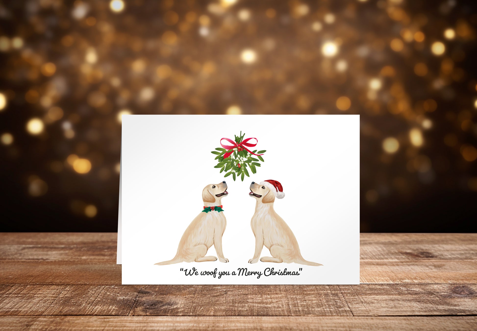 Christmas card with two cream Labrador dogs sitting underneath a mistletoe wreath on a white background, with the text: "We woof you a Merry Christmas"