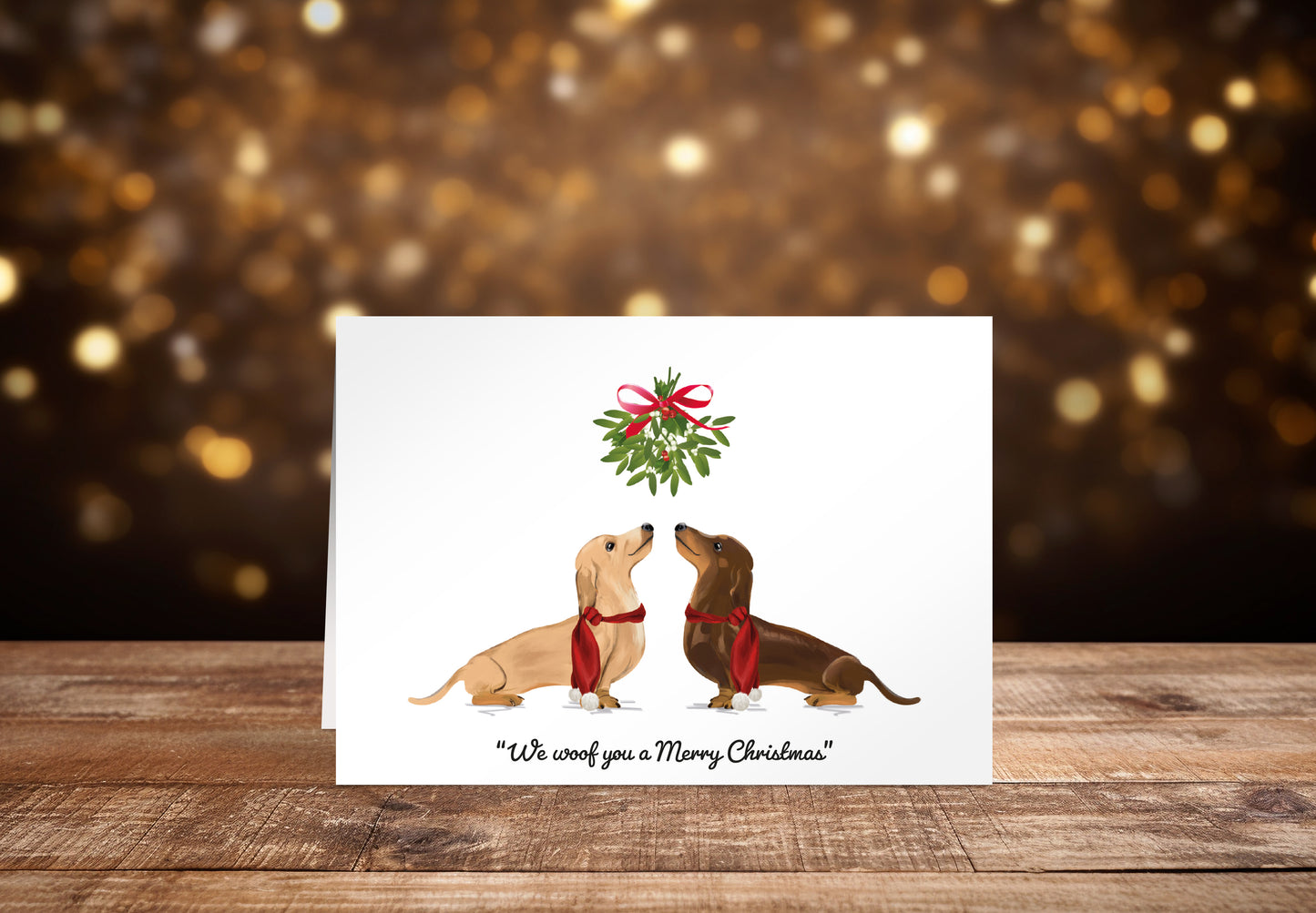 Christmas card with a cream and a brown Dachshund dog underneath mistletoe on a white background with the text "We woof you a Merry Christmas" underneath. 
