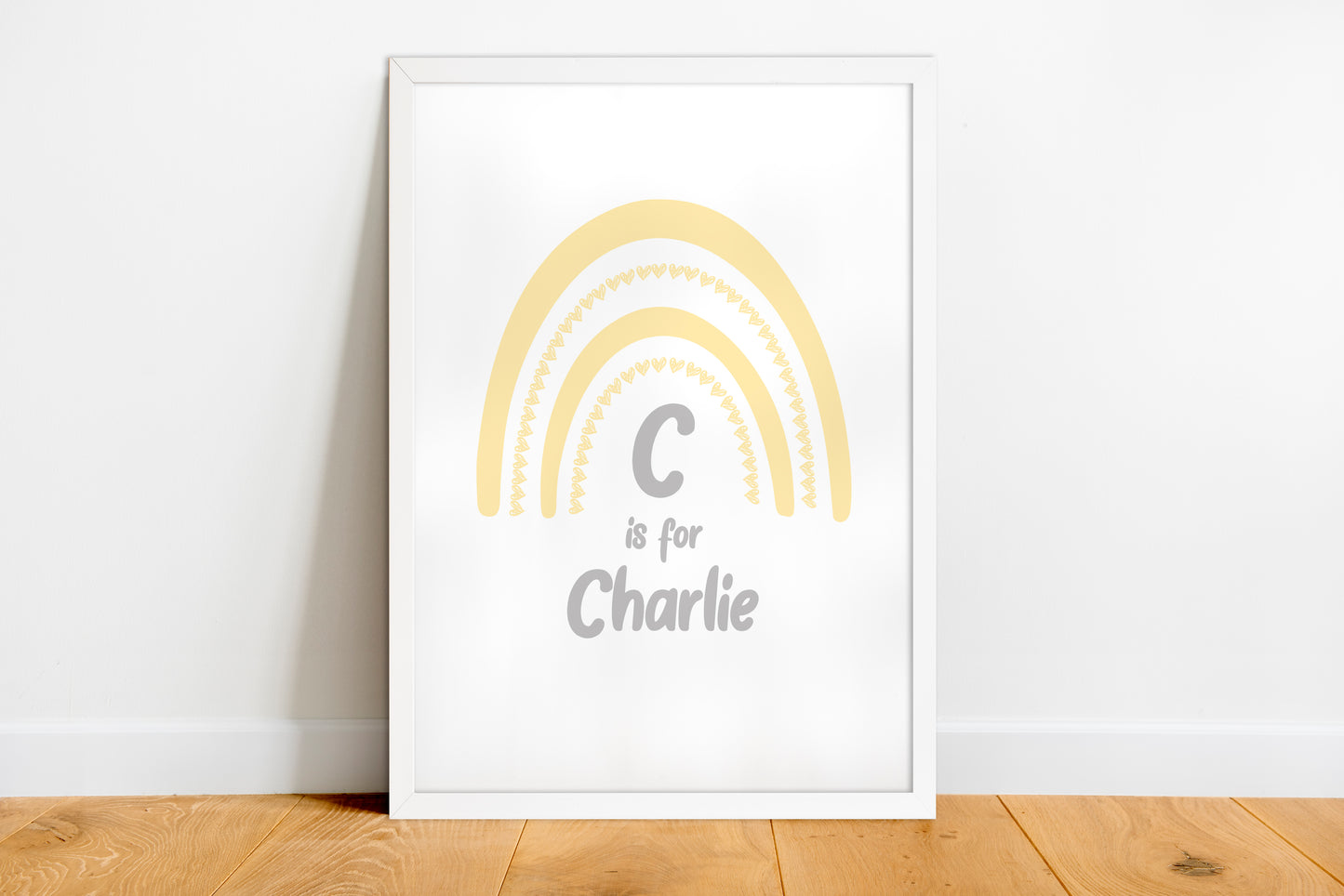 Framed print with a yellow rainbow and text 'C is for Charlie' on a white wall.