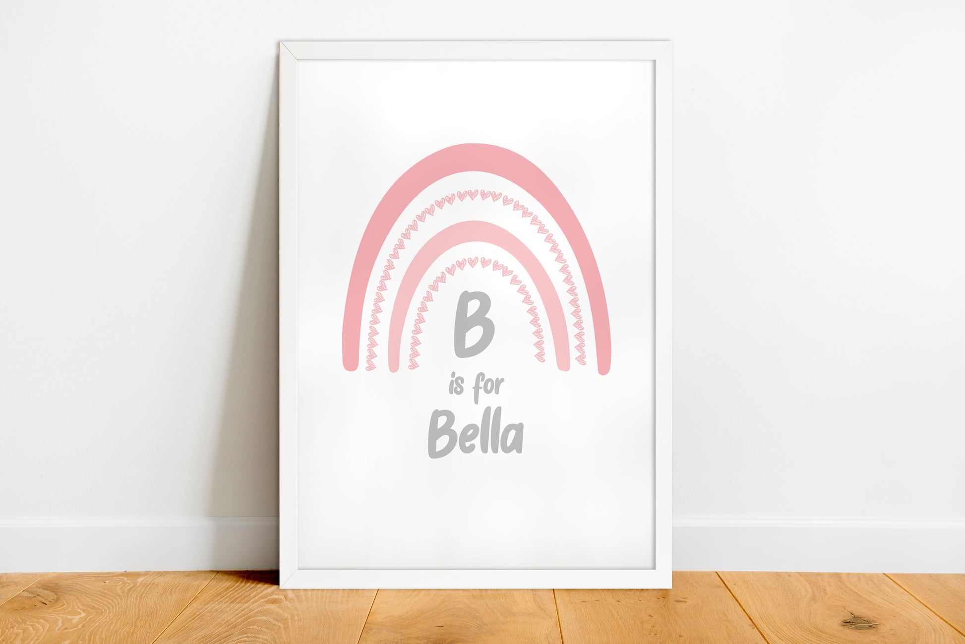 Framed artwork with a pink rainbow and 'B is for Bella' text on a white wall.