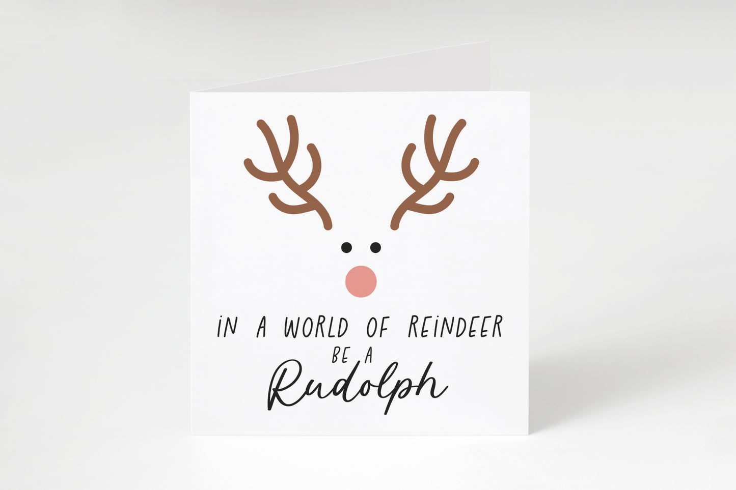 Reindeer face with the text "In a world of reindeer be a Rudolph" on a white square greeting card.