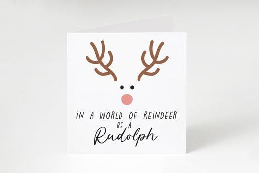 Reindeer face with the text "In a world of reindeer be a Rudolph" on a white square greeting card.